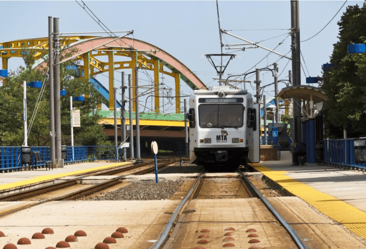 A Baltimore Light Rail train with a bridge in the background.